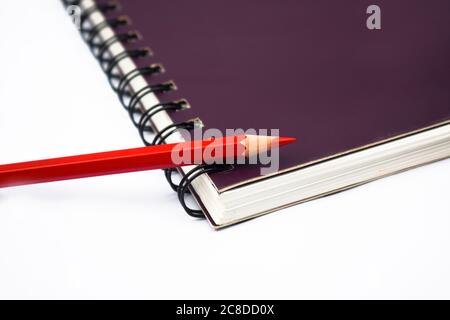 Pastello a matita di legno di colore rosso posto su una carta da libro di note a spirale di colore viola Foto Stock