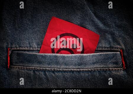 Una faccia triste che si stacca fuori da una tasca dei jeans. Primo piano. Foto Stock