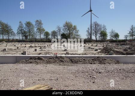 Pali di calcestruzzo prefabbricati quadrati in un luogo di costruzione. Condotto a suolo usando macchina di palo di calcestruzzo. In lontananza un moderno mulino a vento. Alkmaar. Olanda Foto Stock