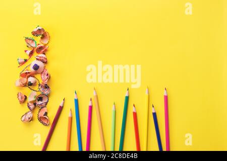 Matite e trucioli di colore su sfondo giallo brillante con copyspace per il testo. Concetto di ritorno a scuola o formazione, focus selettivo. Opuscolo Foto Stock