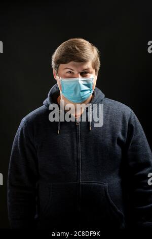 Uomo negli anni '20 con una maschera medica blu in studio. Maschera per fermare la diffusione del coronavirus covid-19 Foto Stock