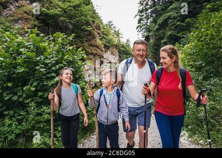 Sorridenti genitori e i loro due figli carini camminano insieme su un sentiero attraverso una valle in una foresta Foto Stock