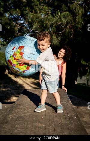 Madre sorridente che guarda il figlio che gioca con il globo sul tavolo Foto Stock