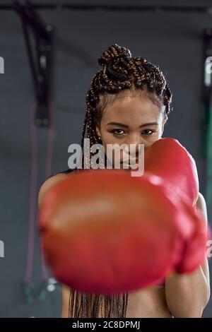 Giovane donna sicura che indossa guanti rossi da boxe che si allenano in palestra Foto Stock
