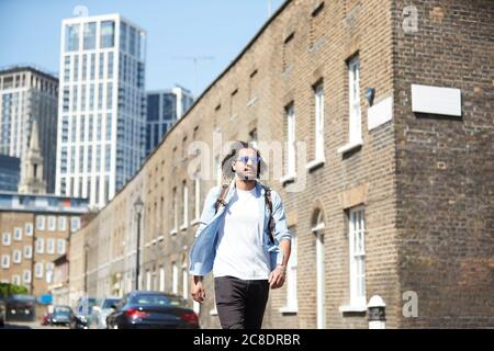 Ritratto di giovane uomo con zaino che cammina su una strada residenziale, Londra, Regno Unito Foto Stock