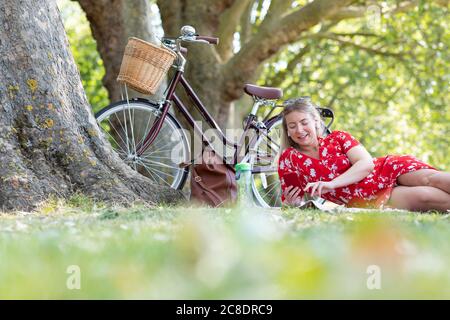 Bella donna che usa lo smartphone mentre si sdraiava nel parco pubblico Foto Stock