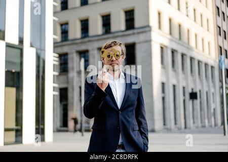 Uomo d'affari che indossa 2020 occhiali da commedia in città dando il dito Foto Stock