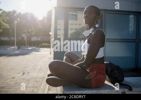 Giovane donna che guarda via mentre si siede sul muro di ritegno dentro città durante il giorno di sole Foto Stock