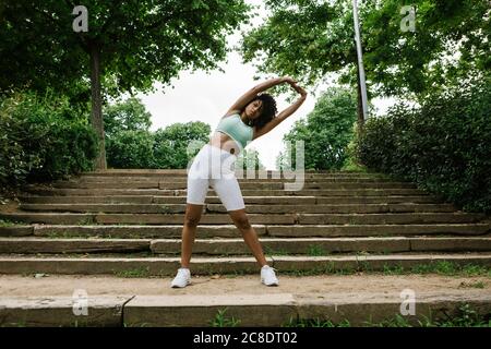 Giovane donna atletica che allunga le braccia sui gradini Foto Stock