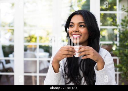 La giovane donna premurosa sorride mentre tiene una tazza di caffè al caffè Foto Stock