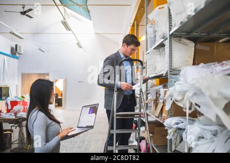 Uomo d'affari su scala e dipendente femminile con laptop in un magazzino Foto Stock