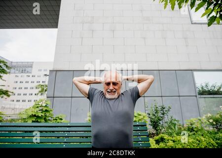 Uomo anziano con armi sollevate che si esercita contro la costruzione in città Foto Stock
