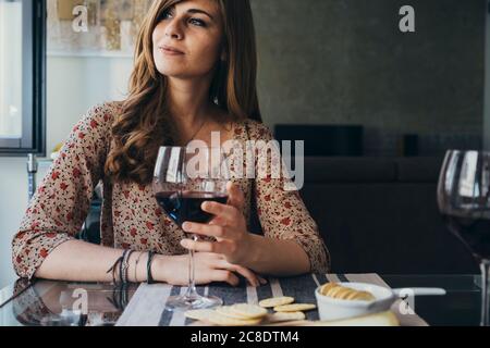 Bella giovane donna che tiene il wineglass che guarda via mentre si siede a. tavolo da pranzo Foto Stock