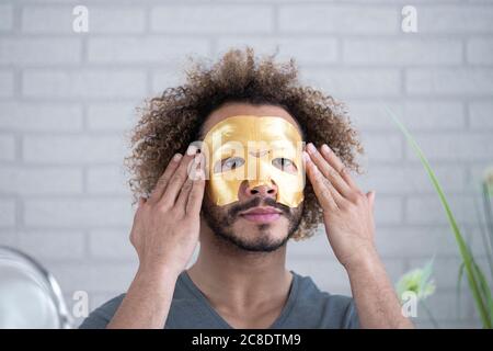 Primo piano di un giovane uomo che applica la maschera facciale a casa Foto Stock