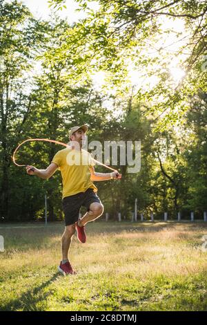 Uomo felice di esercitarsi con corda di salto contro gli alberi al parco Foto Stock