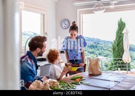 Donna felice che guarda il figlio seduto con l'uomo in cucina Foto Stock