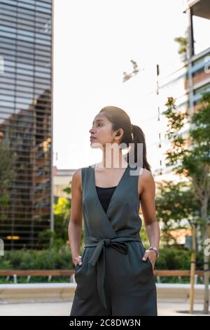 Donna d'affari premurosa con le mani in tasche che guardano via mentre in piedi all'aperto Foto Stock