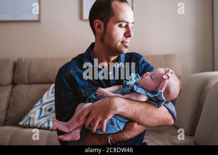 Padre che porta la bambina addormentata sul divano a casa Foto Stock