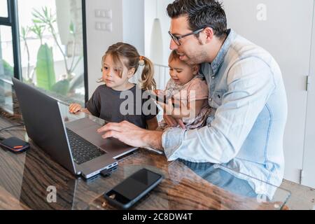 Uomo medio adulta che lavora su un computer portatile con la cura di figlie a casa Foto Stock