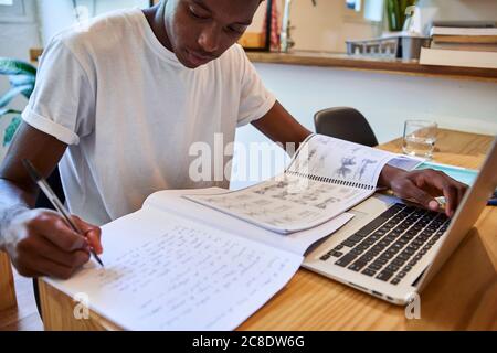 Primo piano del giovane uomo che scrive le sue note nel libro sopra tavolo a casa Foto Stock