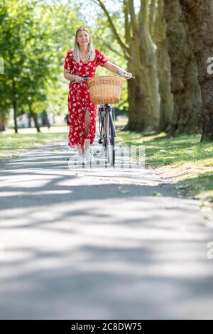 Donna felice a piedi con la bicicletta sul sentiero nel parco pubblico durante il giorno di sole Foto Stock