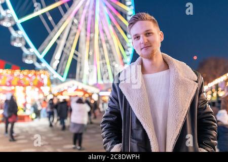 Sorridente bell'uomo in piedi contro ruota panoramica illuminata nel divertimento parcheggia di notte Foto Stock