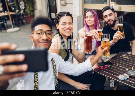 Amici felici che prendono gli occhiali da birra e che prendono un selfie all'aperto in un bar Foto Stock