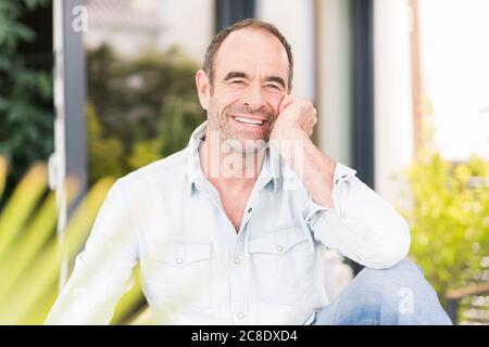 Uomo maturo sorridente seduto al cortile posteriore Foto Stock