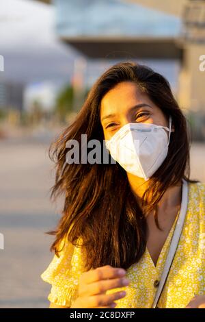 Felice giovane donna che indossa la maschera facciale in città Foto Stock