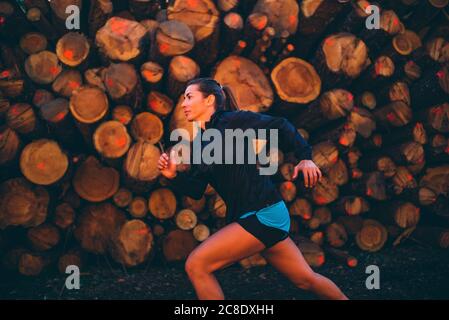 Donna che corre contro i log nella foresta Foto Stock