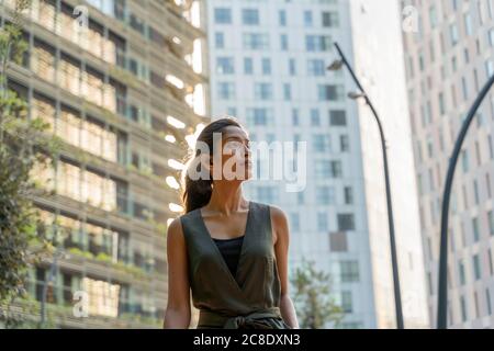 Donna premurosa che guarda lontano mentre si sta in piedi contro gli edifici moderni Foto Stock