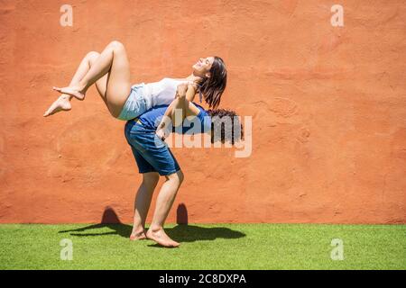 Giovane uomo che porta la donna sulla parte posteriore da parete marrone durante giorno di sole Foto Stock