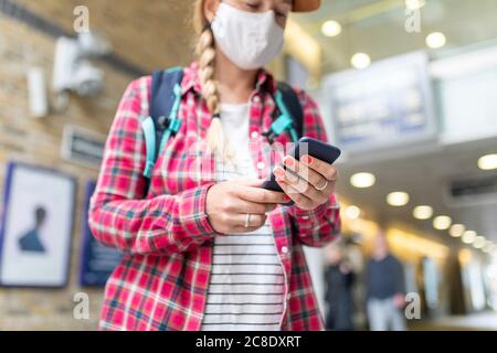 Primo piano della donna che indossa la maschera utilizzando lo smartphone mentre si è in piedi alla stazione della metropolitana Foto Stock