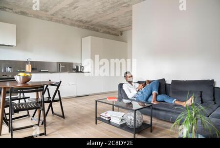 Uomo seduto sul divano in un appartamento moderno con smartphone Foto Stock