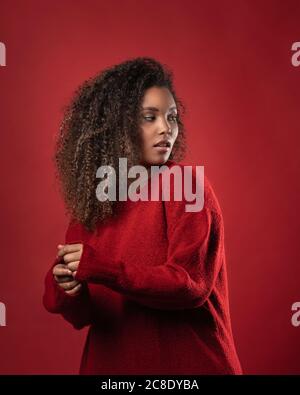 Donna seria premurosa con capelli ricci in piedi su sfondo rosso Foto Stock