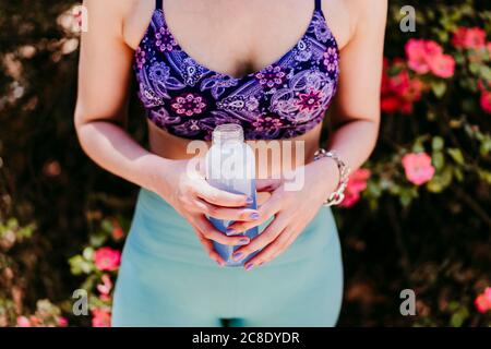Sportivo da donna holding di acqua in bottiglia in posizione di parcheggio Foto Stock