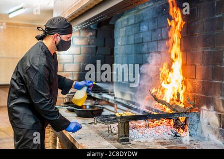 Cucina tradizionale di paella in cucina ristorante, chef con maschera protettiva Foto Stock