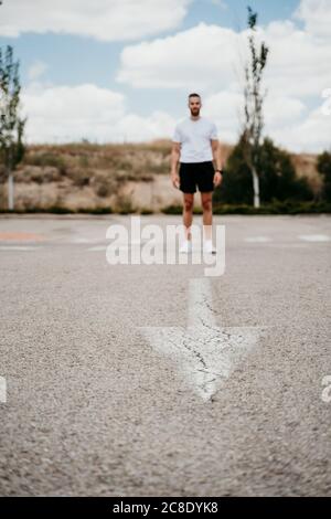 Atleta maschile in piedi al segno freccia sulla strada Foto Stock