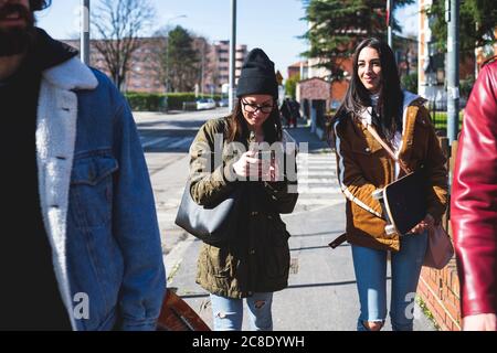 Donna che usa lo smartphone mentre cammina con gli amici sul marciapiede in città Foto Stock