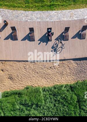 Russia, Tikhvin, uomo in bicicletta sul lungomare con lettini, vista aerea Foto Stock