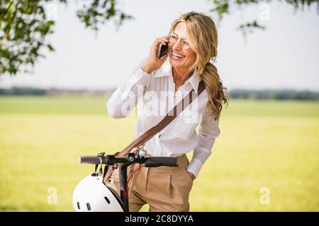 Buon pendolari che usano lo smartphone mentre si è in piedi con la pressione scooter per campo Foto Stock