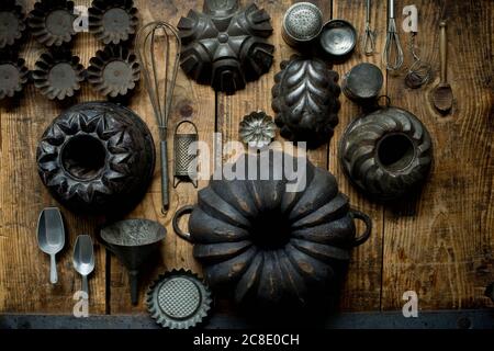 Collezione di vecchi utensili da cucina rustici, tra cui teglie, sessole, grattugia, frusta e imbuto Foto Stock