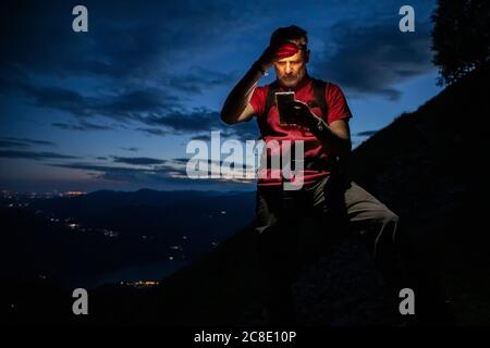 Uomo escursionista controllare mappa su smartphone mentre si trova in montagna di notte, Orobie, Lecco, Italia Foto Stock