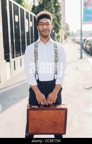 Ritratto di un giovane uomo d'affari sicuro e alla moda che tiene la valigetta la città Foto Stock