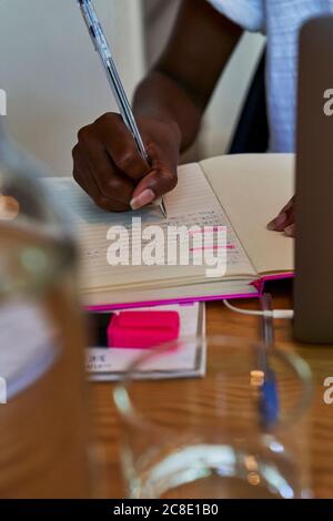 Primo piano di una mano di giovane donna che scrive le note nel libro sopra tavolo a casa Foto Stock