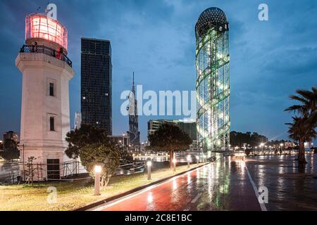 Georgia, Adjara, Batumi, Road di fronte al faro illuminato di Batumi e la torre alfabetica al tramonto Foto Stock