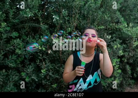 Adolescente ragazza con sindrome di Down indossando 80's colorful make-up e. indumenti che soffiano bolle di sapone Foto Stock