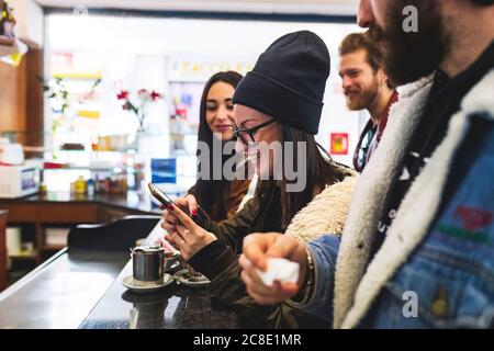 Donna sorridente che usa lo smartphone mentre si divergono con gli amici caffè Foto Stock