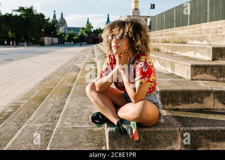 Donna trendy premurosa seduta sui gradini della città Foto Stock