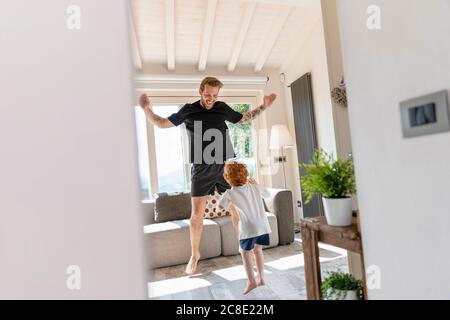 Il padre e il figlio allegri saltano mentre giocano in salotto a casa Foto Stock